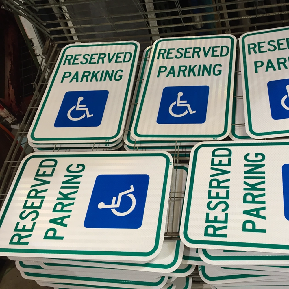 Stacks of finished R7-8 Reserved Parking signs with green text, green borders, and blue International Symbol of Accessibility on white retroreflective sheeting displayed on wire storage racks at the Rice Signs facility.