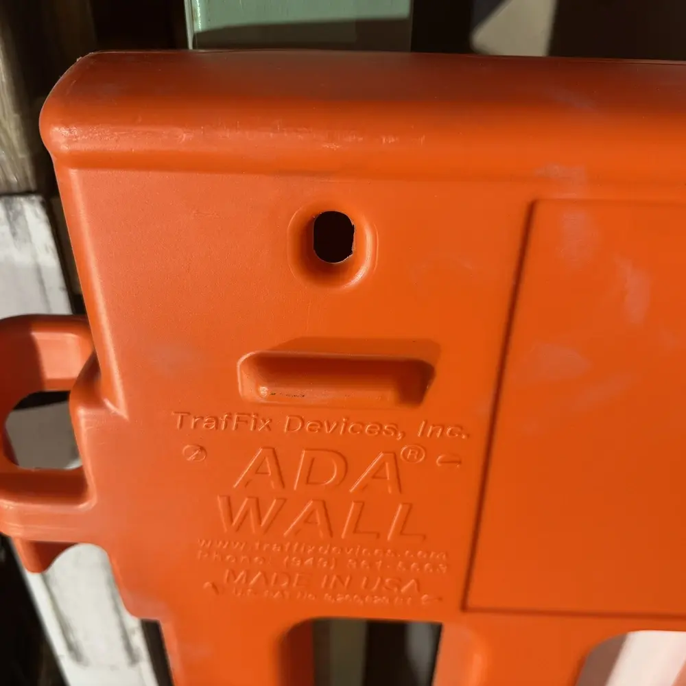 Close-up of the upper corner of a TrafFix Devices, Inc. ADA Wall pedestrian barricade showing the barricade light mounting hole and keyhole slot for attaching warning lights, with molded branding reading 'TrafFix Devices, Inc.,' 'ADA WALL,'