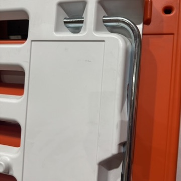 Close-up of the retractable metal support leg on a TrafFix ADA Wall pedestrian barricade, showing the chrome L-shaped leg in the folded-up storage position against the white back panel of the orange barrier.