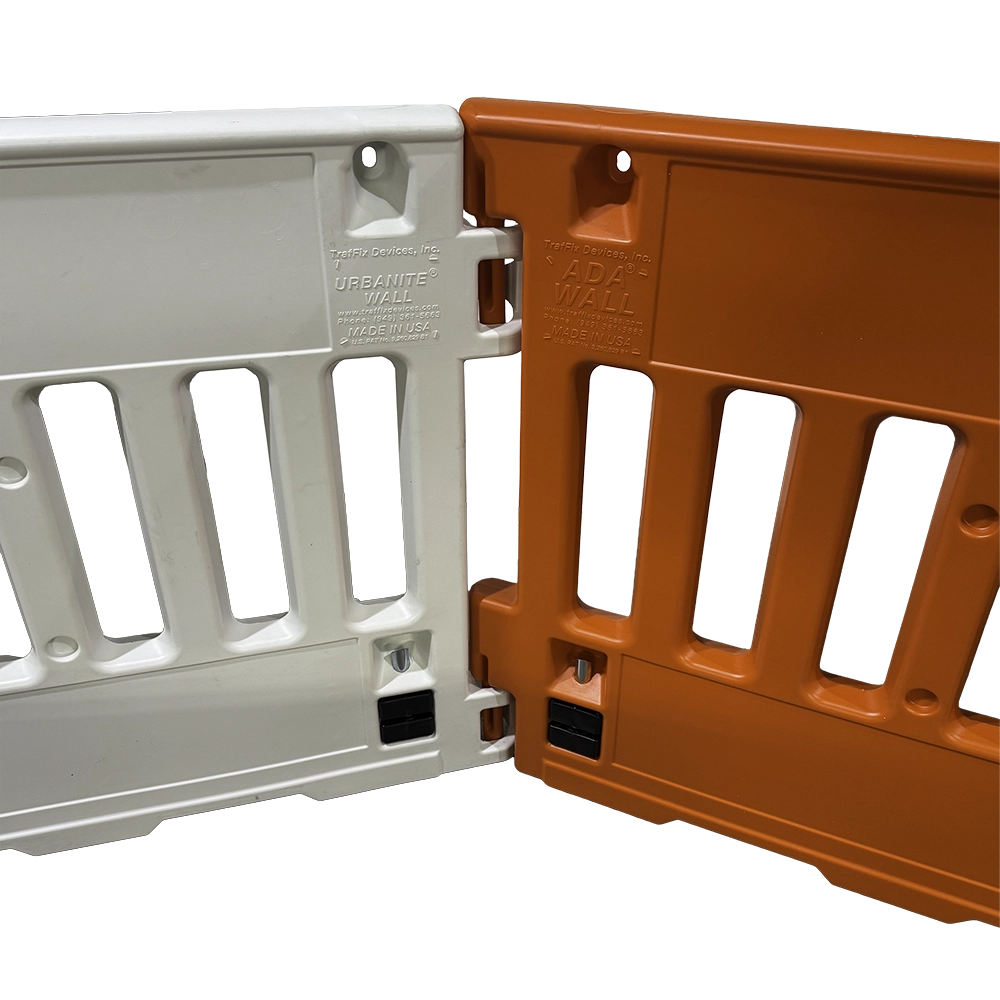 The image shows two rectangular plastic pedestrian barricades connected at their interlocking ends — a white Urbanite Wall on the left and an orange ADA Wall on the right — each with a solid upper rail, slatted middle section with vertical openings, and a solid lower panel. Molded text on the white unit reads 'URBANITE WALL' and on the orange unit reads 'ADA WALL,' both with 'TrafFix Devices, Inc.,' website, phone number, and 'MADE IN USA' markings. No reflective sheeting is visible on this rear-facing side, with barricade light mounting holes at the top corners and foldable metal support legs with black rubber feet at the base.
