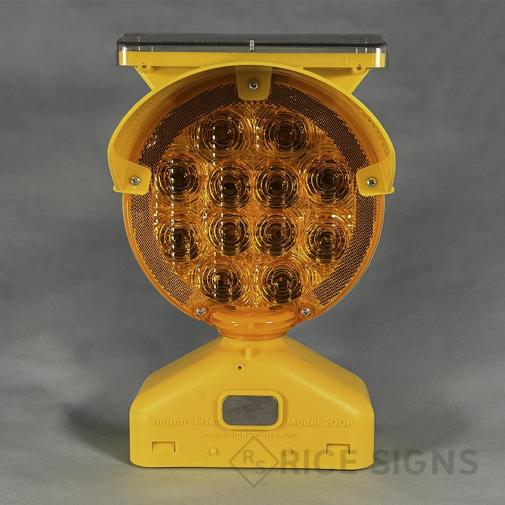 An Empco-Lite Model 2006 solar-powered LED barricade warning light with a large round amber lens containing multiple LED elements, a solar panel mounted on top for charging, and a yellow plastic base with a recessed handle slot for mounting onto barricades and traffic devices.