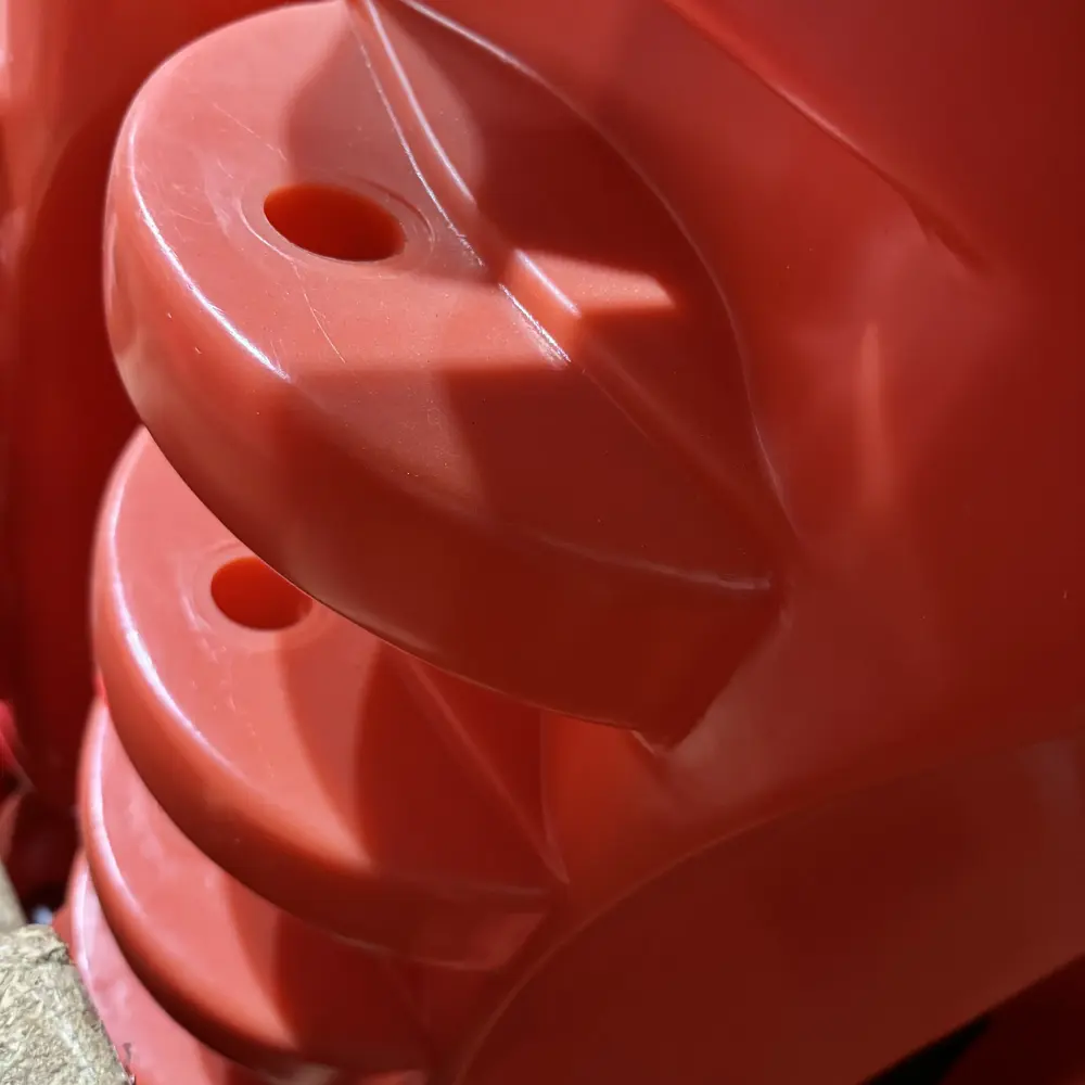 Close-up view of stacked orange water-fill traffic barriers showing the molded interlocking end flanges with connection pin holes used for linking multiple barrier units together in a continuous line.