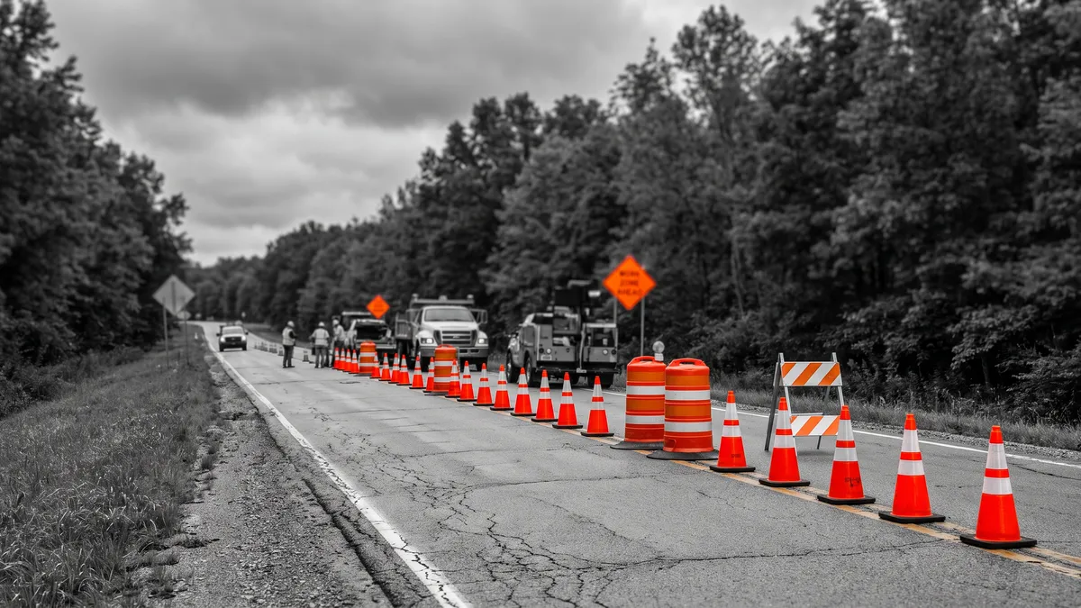 Orange work zone signs, cones, and barricades placed beside a lane closure on a two-lane road.