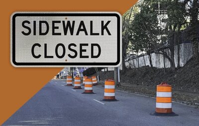 A sidewalk closed sign that is in a workzone with traffic drums