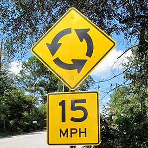 A yellow speed limit 15 mph sign used in a round about.